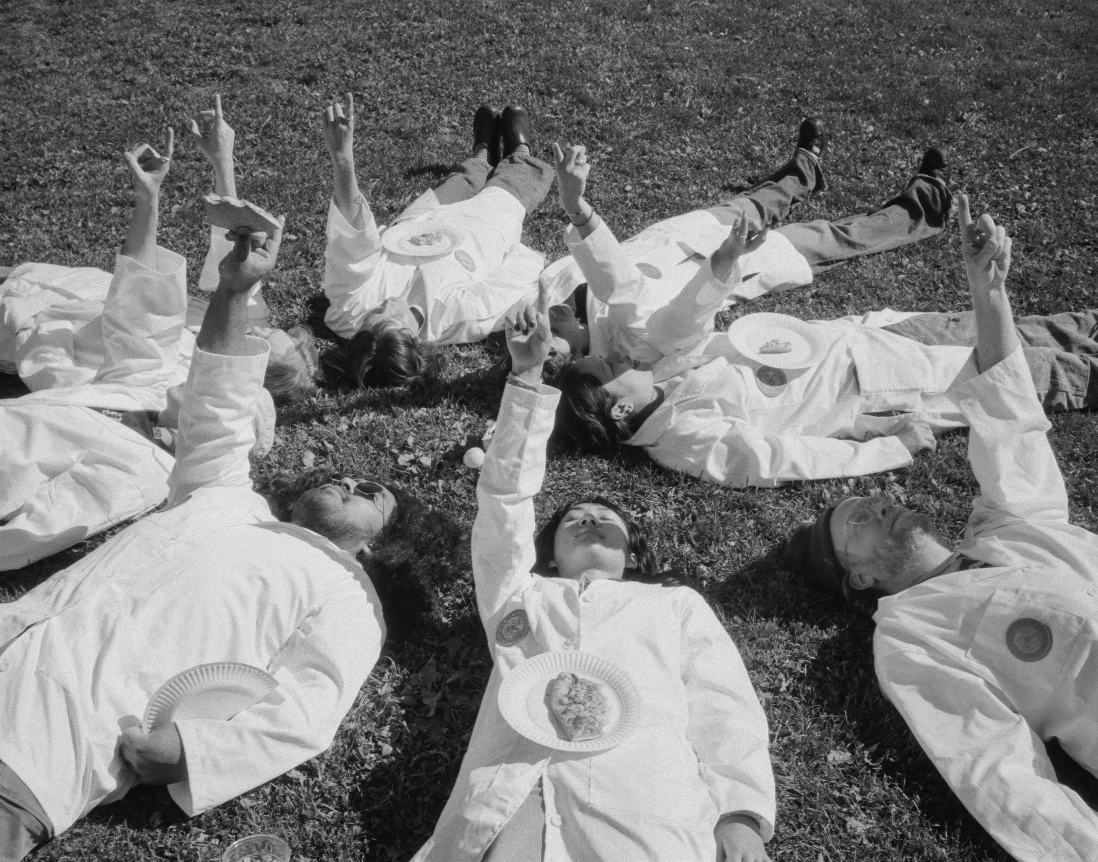 O.S.O. researchers in white lab coats lie on the grass in a circle