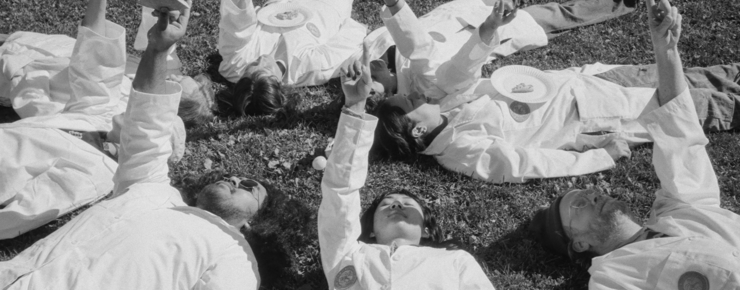 O.S.O. researchers in white lab coats lie on the grass in a circle